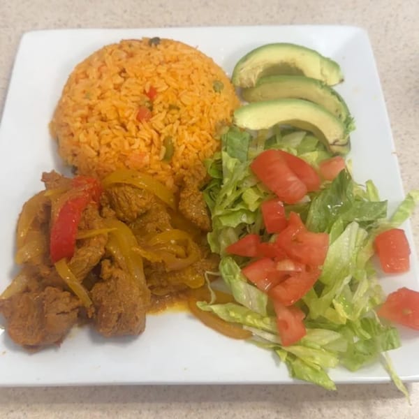 A breakfast plate with seasoned rice, sliced avocado, a side salad, and meat with peppers.