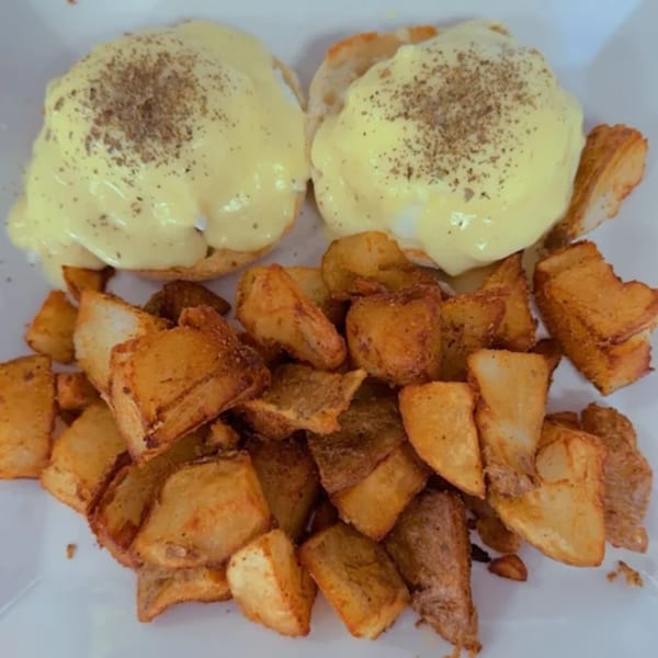 Two eggs Benedict with hollandaise sauce and pepper, served with a side of crispy home fries.