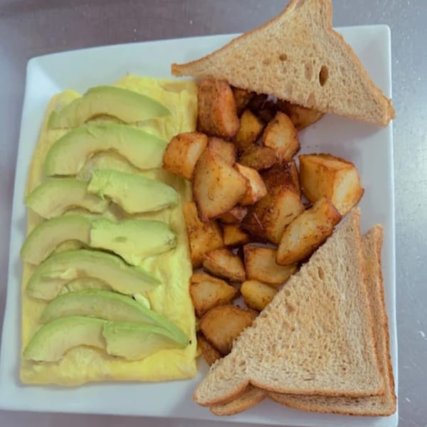 A breakfast plate with an omelet topped with avocado slices, home fries, and wheat toast.