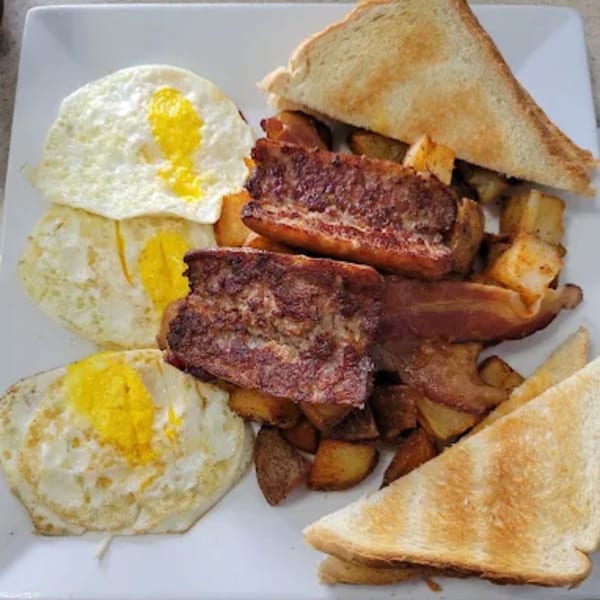 A breakfast plate with three fried eggs, bacon, home fries, and two slices of toast.
